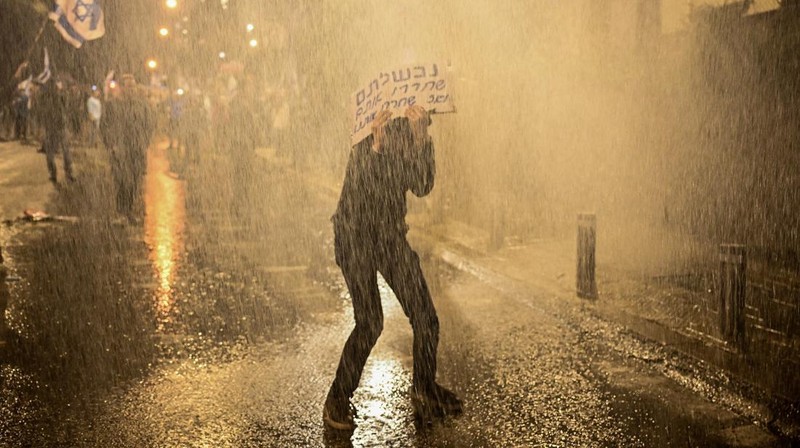 People stand on a street as police use water cannons to disperse demonstrators during a protest against Israeli Prime Minister Benjamin Netanyahu's government, amid the ongoing conflict between Israel and the Palestinian Islamist group Hamas from Gaza, in Tel Aviv, Israel, February 24, 2024. REUTERS/Dylan Martinez