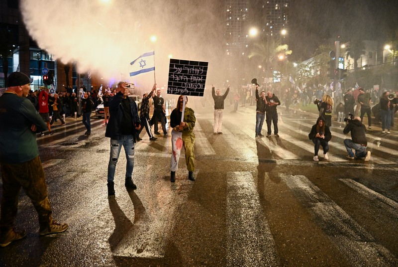ISRAEL-PALESTINIANS/NETANYAHU-PROTEST People stand on a street as police use water cannons to disperse demonstrators during a protest against Israeli Prime Minister Benjamin Netanyahu's government, amid the ongoing conflict between Israel and the Palestinian Islamist group Hamas from Gaza, in Tel Aviv, Israel, February 24, 2024. REUTERS/Dylan Martinez