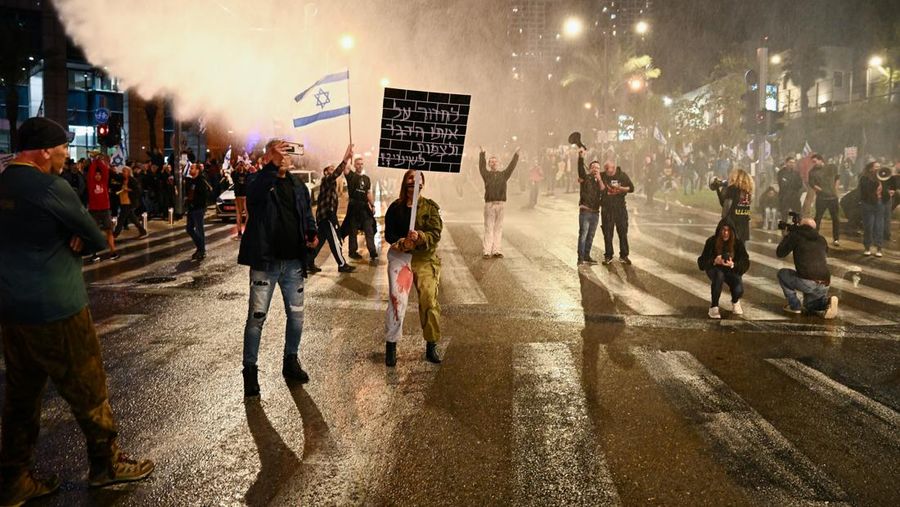 People stand on a street as police use water cannons to disperse demonstrators during a protest against Israeli Prime Minister Benjamin Netanyahu's government, amid the ongoing conflict between Israel and the Palestinian Islamist group Hamas from Gaza, in Tel Aviv, Israel, February 24, 2024. REUTERS/Dylan Martinez