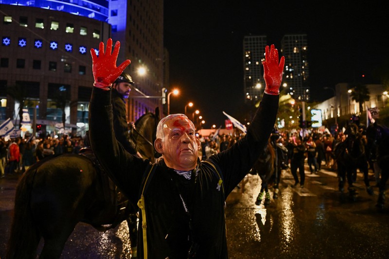 ISRAEL-PALESTINIANS/NETANYAHU-PROTEST People stand on a street as police use water cannons to disperse demonstrators during a protest against Israeli Prime Minister Benjamin Netanyahu's government, amid the ongoing conflict between Israel and the Palestinian Islamist group Hamas from Gaza, in Tel Aviv, Israel, February 24, 2024. REUTERS/Dylan Martinez