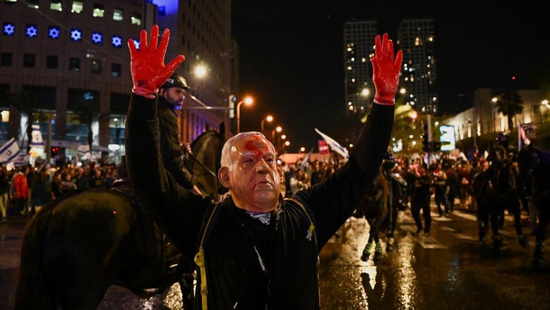 People stand on a street as police use water cannons to disperse demonstrators during a protest against Israeli Prime Minister Benjamin Netanyahu's government, amid the ongoing conflict between Israel and the Palestinian Islamist group Hamas from Gaza, in Tel Aviv, Israel, February 24, 2024. REUTERS/Dylan Martinez