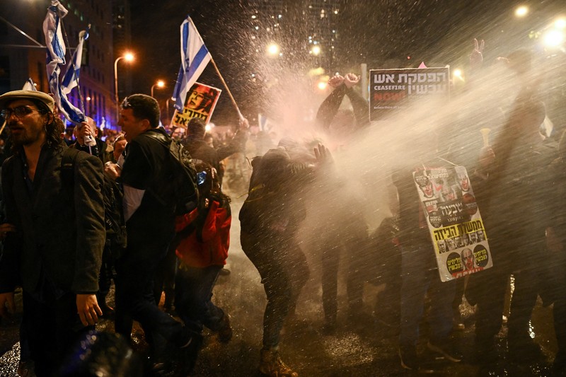 ISRAEL-PALESTINIANS/NETANYAHU-PROTEST People stand on a street as police use water cannons to disperse demonstrators during a protest against Israeli Prime Minister Benjamin Netanyahu's government, amid the ongoing conflict between Israel and the Palestinian Islamist group Hamas from Gaza, in Tel Aviv, Israel, February 24, 2024. REUTERS/Dylan Martinez