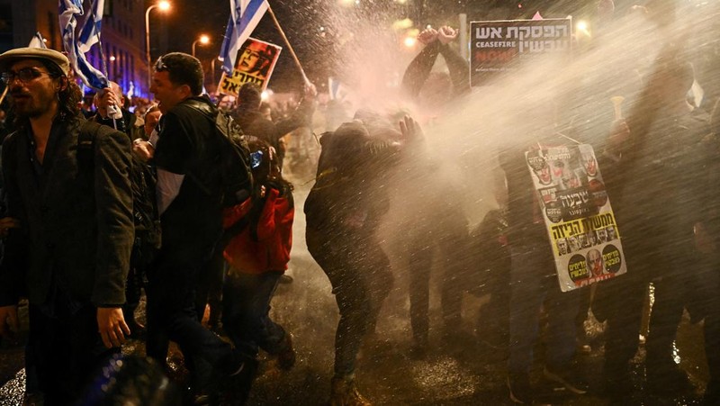 People stand on a street as police use water cannons to disperse demonstrators during a protest against Israeli Prime Minister Benjamin Netanyahu's government, amid the ongoing conflict between Israel and the Palestinian Islamist group Hamas from Gaza, in Tel Aviv, Israel, February 24, 2024. REUTERS/Dylan Martinez