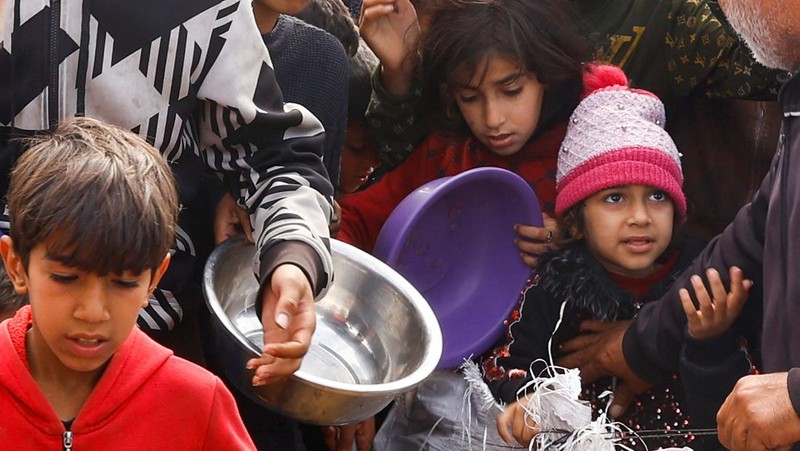 Anak-anak Palestina yang terlantar menunggu untuk menerima makanan gratis di tenda kamp, ​​di tengah kekurangan makanan, saat konflik antara Israel dan Hamas berlanjut, di Rafah di selatan Jalur Gaza, 27 Februari 2024. (REUTERS/Ibraheem Abu Mustafa)
