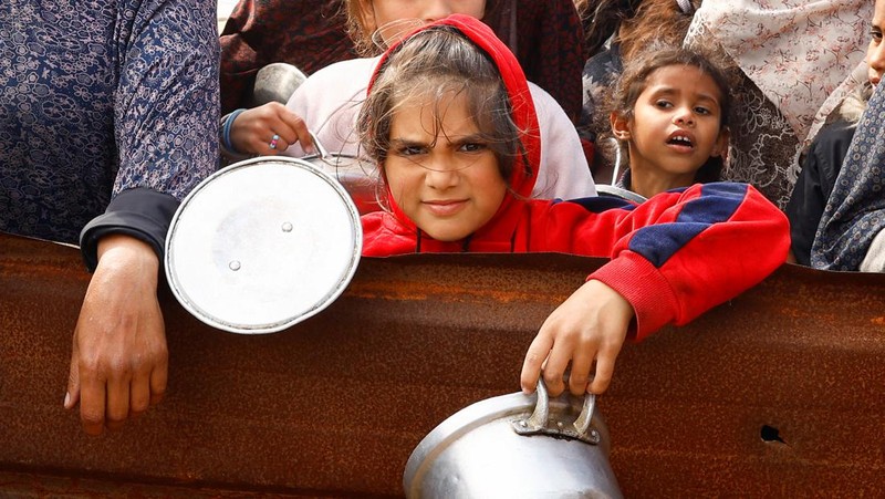 Anak-anak Palestina yang terlantar menunggu untuk menerima makanan gratis di tenda kamp, ​​di tengah kekurangan makanan, saat konflik antara Israel dan Hamas berlanjut, di Rafah di selatan Jalur Gaza, 27 Februari 2024. (REUTERS/Ibraheem Abu Mustafa)