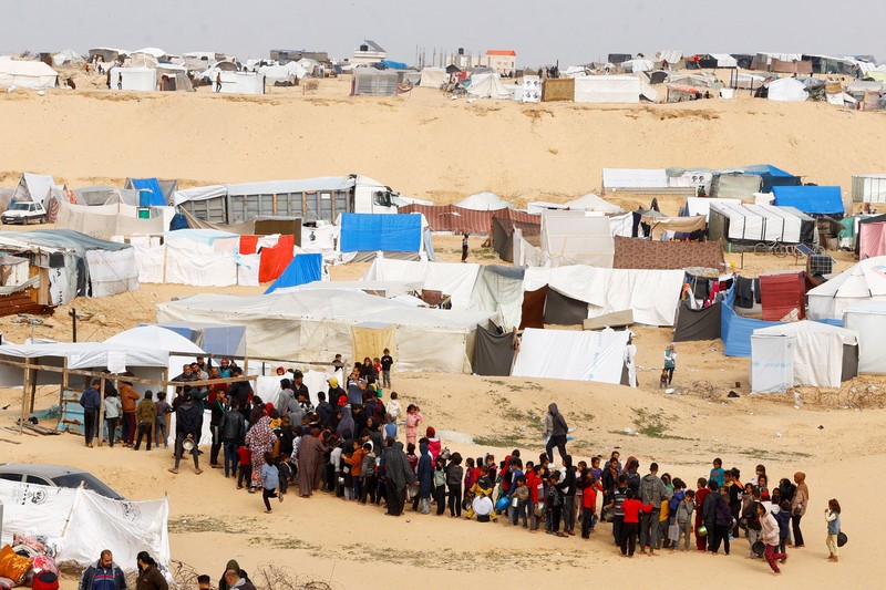 Anak-anak Palestina yang terlantar menunggu untuk menerima makanan gratis di tenda kamp, ​​di tengah kekurangan makanan, saat konflik antara Israel dan Hamas berlanjut, di Rafah di selatan Jalur Gaza, 27 Februari 2024. (REUTERS/Ibraheem Abu Mustafa)