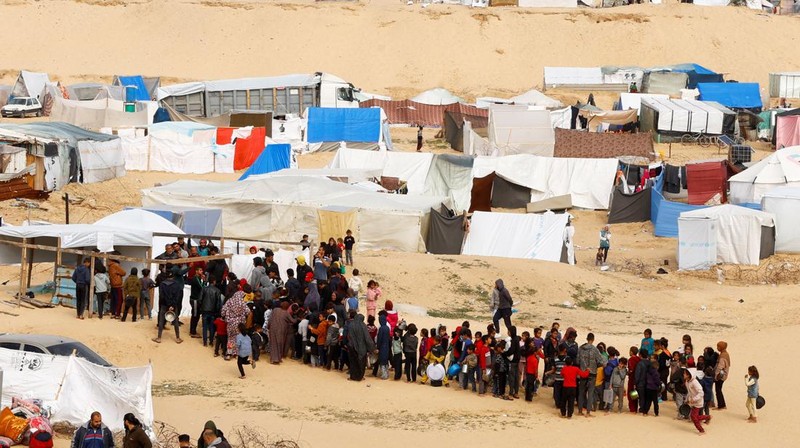 Anak-anak Palestina yang terlantar menunggu untuk menerima makanan gratis di tenda kamp, ​​di tengah kekurangan makanan, saat konflik antara Israel dan Hamas berlanjut, di Rafah di selatan Jalur Gaza, 27 Februari 2024. (REUTERS/Ibraheem Abu Mustafa)