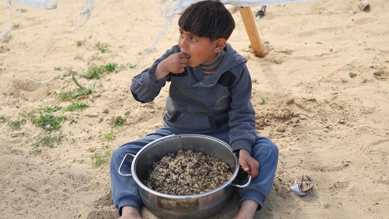 Anak-anak Palestina yang terlantar menunggu untuk menerima makanan gratis di tenda kamp, ​​di tengah kekurangan makanan, saat konflik antara Israel dan Hamas berlanjut, di Rafah di selatan Jalur Gaza, 27 Februari 2024. (REUTERS/Ibraheem Abu Mustafa)