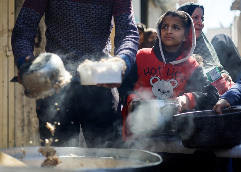 Anak-anak Palestina menunggu untuk menerima makanan yang dimasak oleh dapur amal di tengah kekurangan pasokan makanan, ketika konflik yang sedang berlangsung antara Israel dan kelompok Islam Palestina Hamas berlanjut, di Rafah, di selatan Jalur Gaza, 5 Maret 2024. (REUTERS/Mohammed Salem)