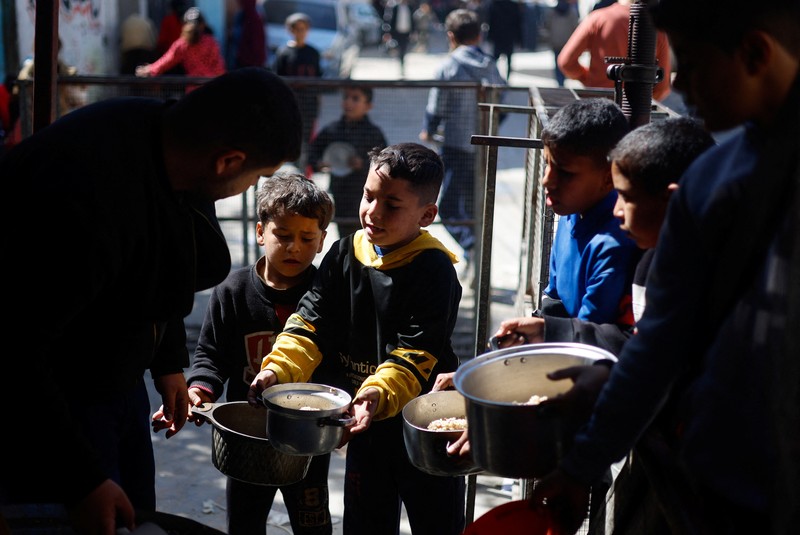 Anak-anak Palestina menunggu untuk menerima makanan yang dimasak oleh dapur amal di tengah kekurangan pasokan makanan, ketika konflik yang sedang berlangsung antara Israel dan kelompok Islam Palestina Hamas berlanjut, di Rafah, di selatan Jalur Gaza, 5 Maret 2024. (REUTERS/Mohammed Salem)