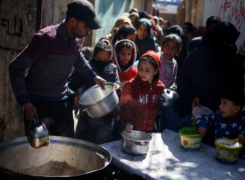 Anak-anak Palestina menunggu untuk menerima makanan yang dimasak oleh dapur amal di tengah kekurangan pasokan makanan, ketika konflik yang sedang berlangsung antara Israel dan kelompok Islam Palestina Hamas berlanjut, di Rafah, di selatan Jalur Gaza, 5 Maret 2024. (REUTERS/Mohammed Salem)