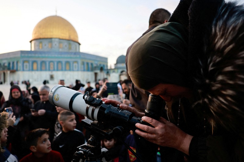 Anggota Masyarakat Astronomi Palestina dan tim Wakaf menggunakan teleskop untuk mencari bulan sabit menjelang bulan suci Ramadhan, di kompleks Al-Aqsa, yang dikenal oleh orang Yahudi sebagai Temple Mount, di Kota Tua Yerusalem 10 Maret 2024. (REUTERS/Ammar Awad)