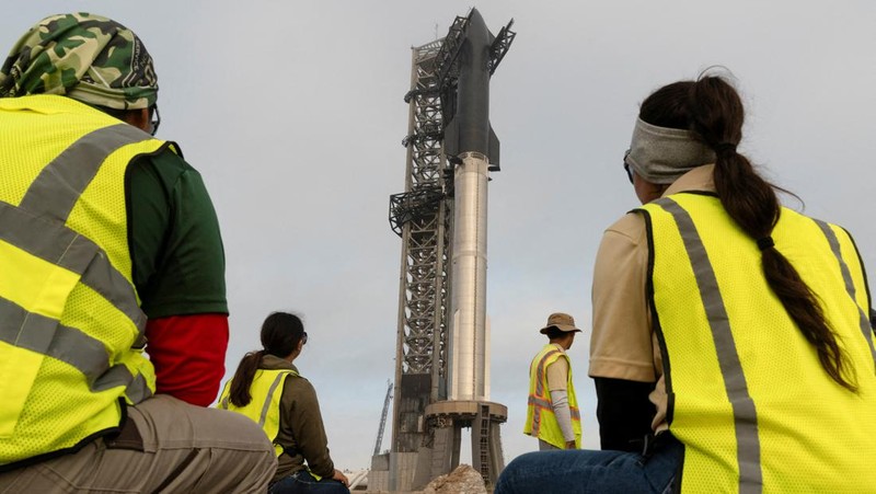 Para pekerja beristirahat sambil memindahkan bebatuan dan puing-puing dari area sekitar saat pesawat luar angkasa Starship generasi berikutnya milik SpaceX yang berada di atas roket Super Heavy. (REUTERS/Cheney Orr)