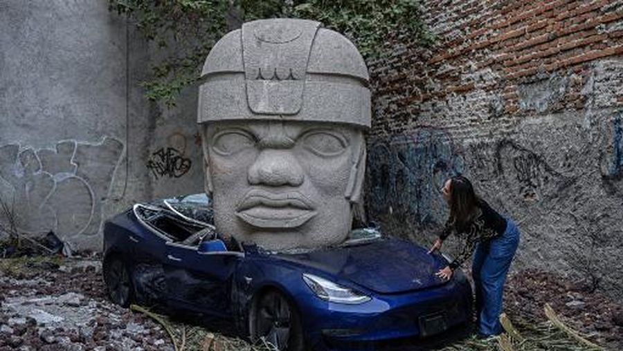 An artwork by artist Chavis Marmol, a Tesla 3 car crushed by a nine-ton Olmec-inspired head, is pictured in Mexico City on March 13, 2024. A 42-year-old sculptor, Marmol has never owned a car and travels by bicycle, but he had the luxury of unloading with cranes the nine-ton effigy on a blue Tesla 3, one of the electric models manufactured by US billionaire Elon Musk's company. (Photo by CARL DE SOUZA / AFP) / RESTRICTED TO EDITORIAL USE - MANDATORY MENTION OF THE ARTIST UPON PUBLICATION - TO ILLUSTRATE THE EVENT AS SPECIFIED IN THE CAPTION
