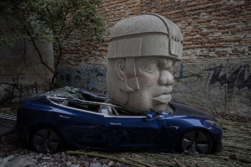 An artwork by artist Chavis Marmol, a Tesla 3 car crushed by a nine-ton Olmec-inspired head, is pictured in Mexico City on March 13, 2024. A 42-year-old sculptor, Marmol has never owned a car and travels by bicycle, but he had the luxury of unloading with cranes the nine-ton effigy on a blue Tesla 3, one of the electric models manufactured by US billionaire Elon Musk's company. (Photo by CARL DE SOUZA / AFP) / RESTRICTED TO EDITORIAL USE - MANDATORY MENTION OF THE ARTIST UPON PUBLICATION - TO ILLUSTRATE THE EVENT AS SPECIFIED IN THE CAPTION