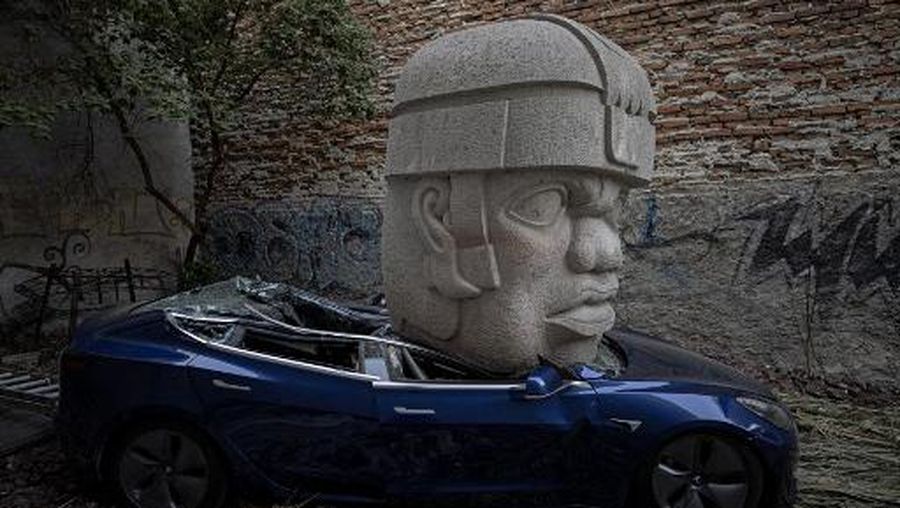 An artwork by artist Chavis Marmol, a Tesla 3 car crushed by a nine-ton Olmec-inspired head, is pictured in Mexico City on March 13, 2024. A 42-year-old sculptor, Marmol has never owned a car and travels by bicycle, but he had the luxury of unloading with cranes the nine-ton effigy on a blue Tesla 3, one of the electric models manufactured by US billionaire Elon Musk's company. (Photo by CARL DE SOUZA / AFP) / RESTRICTED TO EDITORIAL USE - MANDATORY MENTION OF THE ARTIST UPON PUBLICATION - TO ILLUSTRATE THE EVENT AS SPECIFIED IN THE CAPTION