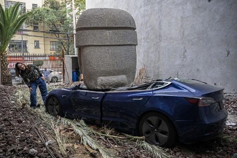An artwork by artist Chavis Marmol, a Tesla 3 car crushed by a nine-ton Olmec-inspired head, is pictured in Mexico City on March 13, 2024. A 42-year-old sculptor, Marmol has never owned a car and travels by bicycle, but he had the luxury of unloading with cranes the nine-ton effigy on a blue Tesla 3, one of the electric models manufactured by US billionaire Elon Musk's company. (Photo by CARL DE SOUZA / AFP) / RESTRICTED TO EDITORIAL USE - MANDATORY MENTION OF THE ARTIST UPON PUBLICATION - TO ILLUSTRATE THE EVENT AS SPECIFIED IN THE CAPTION