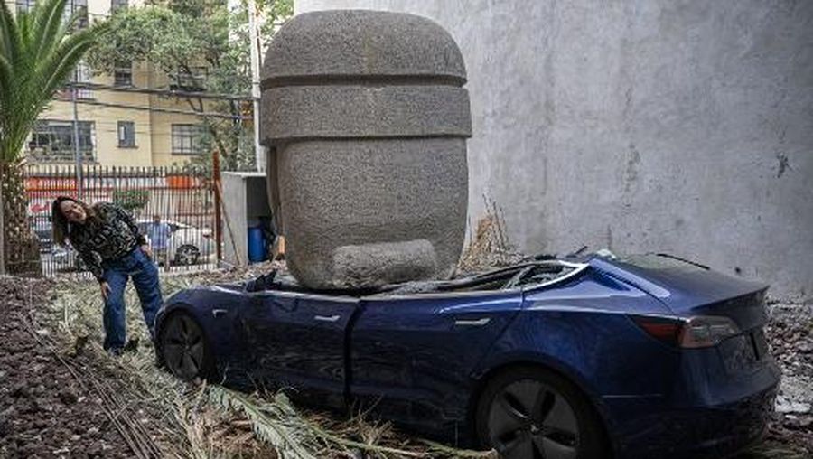 An artwork by artist Chavis Marmol, a Tesla 3 car crushed by a nine-ton Olmec-inspired head, is pictured in Mexico City on March 13, 2024. A 42-year-old sculptor, Marmol has never owned a car and travels by bicycle, but he had the luxury of unloading with cranes the nine-ton effigy on a blue Tesla 3, one of the electric models manufactured by US billionaire Elon Musk's company. (Photo by CARL DE SOUZA / AFP) / RESTRICTED TO EDITORIAL USE - MANDATORY MENTION OF THE ARTIST UPON PUBLICATION - TO ILLUSTRATE THE EVENT AS SPECIFIED IN THE CAPTION