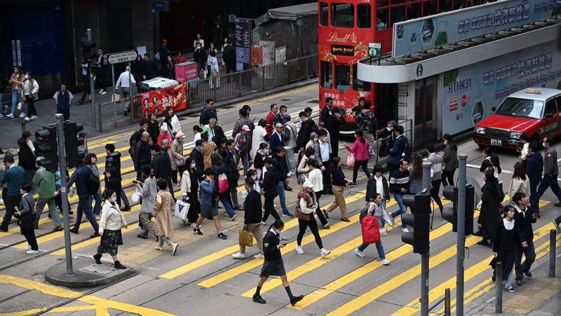 Orang-orang melintasi persimpangan di kawasan pusat bisnis Hong Kong pada 27 Februari 2024, sehari sebelum anggaran tahunan kota tersebut diumumkan pada 28 Februari. (Photo by Peter PARKS / AFP)
