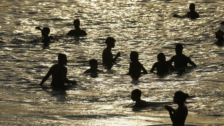 Orang-orang nongkrong di perairan dangkal pantai Arpoador di tengah gelombang panas, di Rio de Janeiro, Brasil, Rabu, 20 Maret 2024. (AP Photo/Silvia Izquierdo)