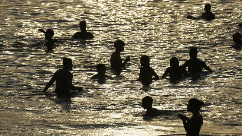 Orang-orang nongkrong di perairan dangkal pantai Arpoador di tengah gelombang panas, di Rio de Janeiro, Brasil, Rabu, 20 Maret 2024. (AP Photo/Silvia Izquierdo)