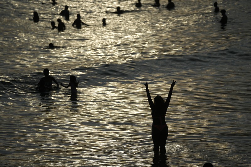 Orang-orang nongkrong di perairan dangkal pantai Arpoador di tengah gelombang panas, di Rio de Janeiro, Brasil, Rabu, 20 Maret 2024. (AP Photo/Silvia Izquierdo)