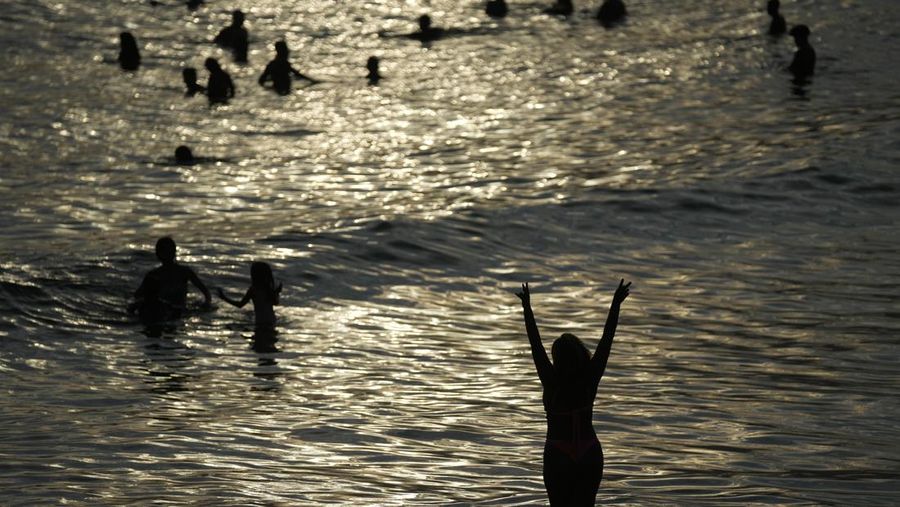 Orang-orang nongkrong di perairan dangkal pantai Arpoador di tengah gelombang panas, di Rio de Janeiro, Brasil, Rabu, 20 Maret 2024. (AP Photo/Silvia Izquierdo)