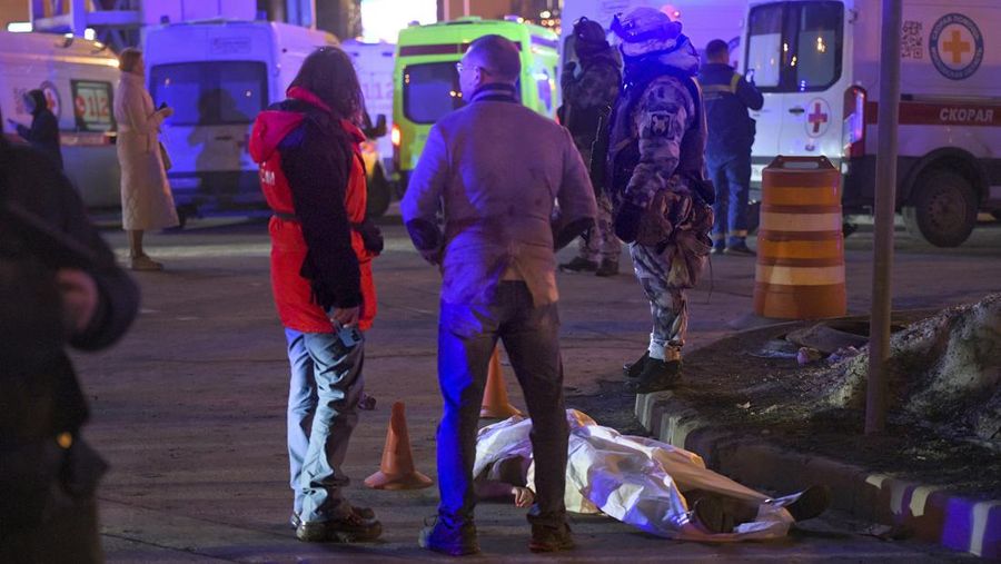 Orang-orang berdiri di depan jenazah korban di dekat gedung Balai Kota Crocus yang terbakar di tepi barat Moskow, Rusia, Jumat, 22 Maret 2024. (AP Photo)