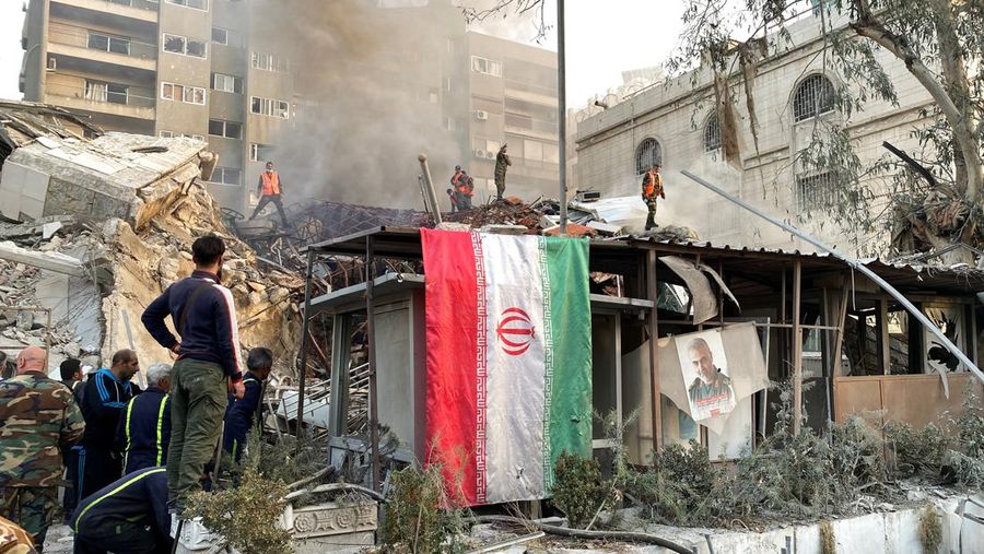 Bendera Iran digantung saat asap mengepul setelah apa yang disebut media Iran sebagai serangan Israel terhadap gedung dekat kedutaan Iran di Damaskus, Suriah 1 April 2024. (REUTERS/Firas Makdesi)
