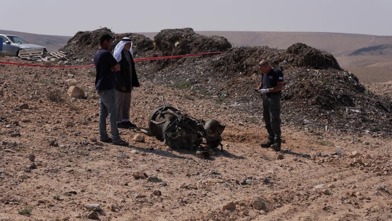 Seorang petugas polisi dan warga memeriksa sisa-sisa pendorong roket yang, menurut pihak berwenang Israel, melukai parah seorang gadis berusia 7 tahun, setelah Iran meluncurkan drone dan rudal ke arah Israel, dekat Arad, Israel, 14 April 2024. (REUTERS/Christophe van der Perre)