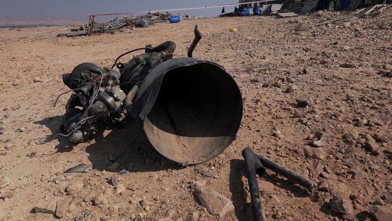 Seorang petugas polisi dan warga memeriksa sisa-sisa pendorong roket yang, menurut pihak berwenang Israel, melukai parah seorang gadis berusia 7 tahun, setelah Iran meluncurkan drone dan rudal ke arah Israel, dekat Arad, Israel, 14 April 2024. (REUTERS/Christophe van der Perre)