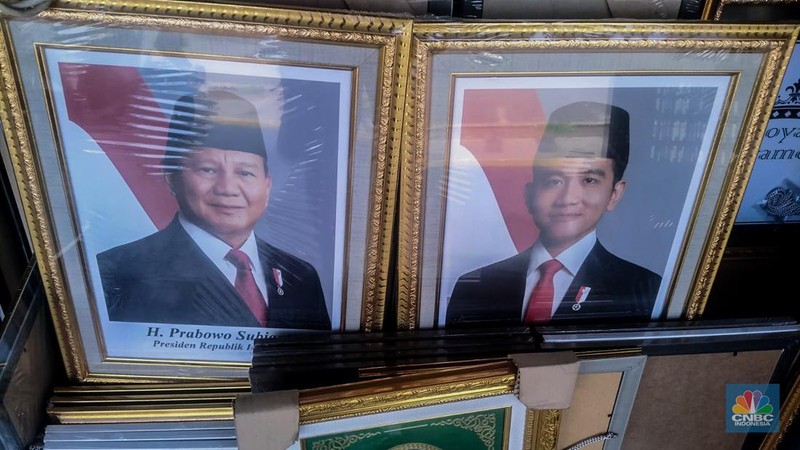 Seorang pedagang menata bingkai foto calon Presiden dan Wakil Presiden terpilih Prabowo Subianto dan Gibran Rakabuming Raka di Kawasan Jalan Jatinegara Jatim, Sabtu (20/4/2024). (CNBC Indonesia/Suhendra)