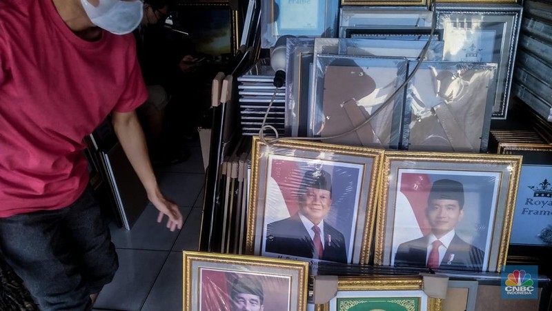 Seorang pedagang menata bingkai foto calon Presiden dan Wakil Presiden terpilih Prabowo Subianto dan Gibran Rakabuming Raka di Kawasan Jalan Jatinegara Jatim, Sabtu (20/4/2024). (CNBC Indonesia/Suhendra)
