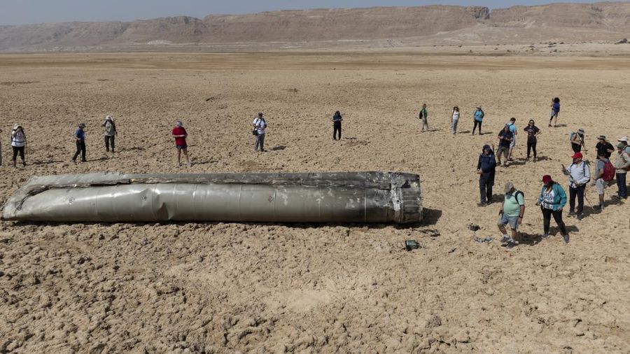 People gather around a component from an intercepted ballistic missile that fell near the Dead Sea in Israel, Saturday, April 20, 2024. Open fighting between Israel and Iran began April 1 with the suspected Israeli killing of Iranian generals at an Iranian diplomatic compound in Syria. That prompted Iran's retaliatory barrage last weekend of more than 300 missiles and drones that the U.S., Israel and regional and international partners helped bat down without significant damage in Israel. And then came Friday's strikes that hit near military and nuclear targets in Iran. (AP Photo/Itamar Grinberg)