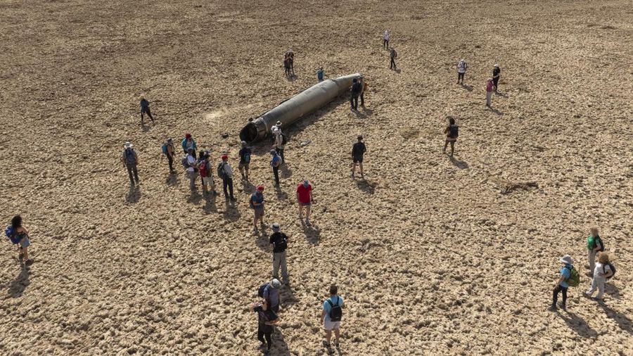 People gather around a component from an intercepted ballistic missile that fell near the Dead Sea in Israel, Saturday, April 20, 2024. Open fighting between Israel and Iran began April 1 with the suspected Israeli killing of Iranian generals at an Iranian diplomatic compound in Syria. That prompted Iran's retaliatory barrage last weekend of more than 300 missiles and drones that the U.S., Israel and regional and international partners helped bat down without significant damage in Israel. And then came Friday's strikes that hit near military and nuclear targets in Iran. (AP Photo/Itamar Grinberg)