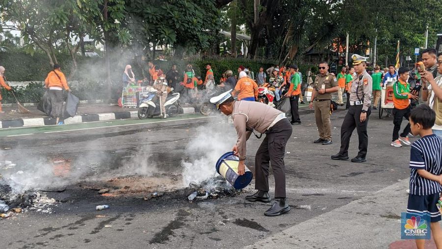 Seorang polisi memadamkan sebuah api yang dibakar oleh massa saat menggelar aksi saat putusan sidang Mahkamah Konstitusi. (CNBC Indonesia/Emir Yanwardhana)