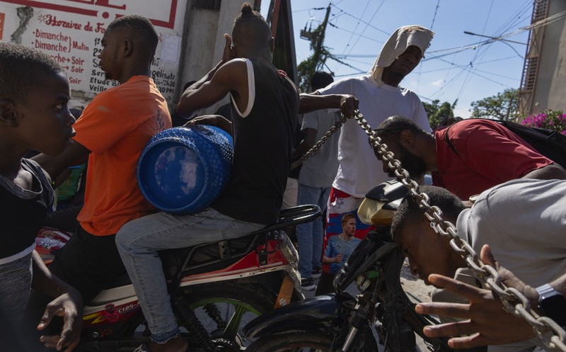 Seorang pria mengangkat rantai yang digunakan sebagai barikade agar tetangga dapat masuk ke lingkungan tersebut saat mereka bekerja menyiapkan gerbang logam untuk melindungi diri dari geng, di lingkungan Petion-Ville di Port-au-Prince, Haiti, Sabtu, 20 April , 2024. (AP Photo/Ramon Espinosa)