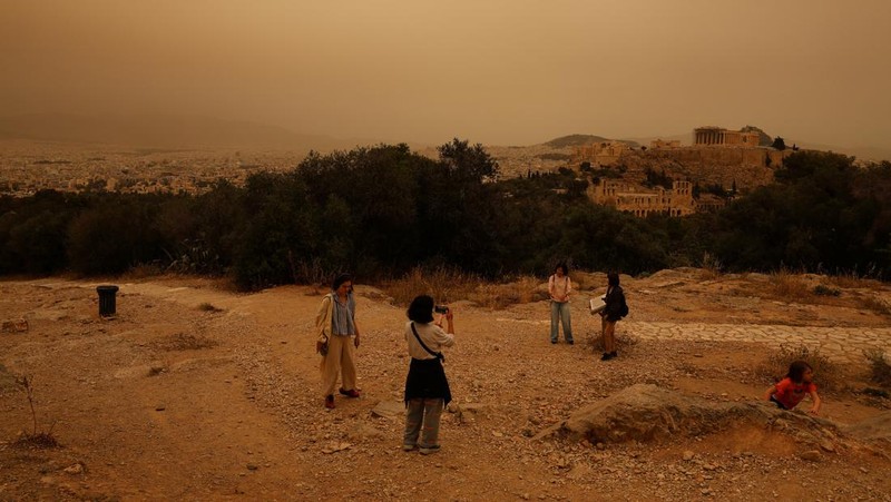 Warga mengabadikan momen gelombang debu yang tertiup angin dari gurun Sahara menutupi Athena dan kota-kota Yunani lainnya pada Selasa, (23/4/2024) waktu setempat. (AP Photo/Petros Giannakouris)