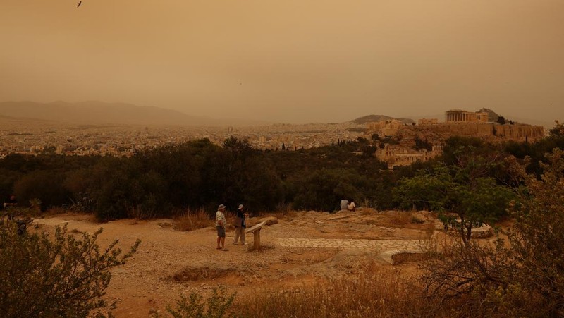 Warga mengabadikan momen gelombang debu yang tertiup angin dari gurun Sahara menutupi Athena dan kota-kota Yunani lainnya pada Selasa, (23/4/2024) waktu setempat. (AP Photo/Petros Giannakouris)