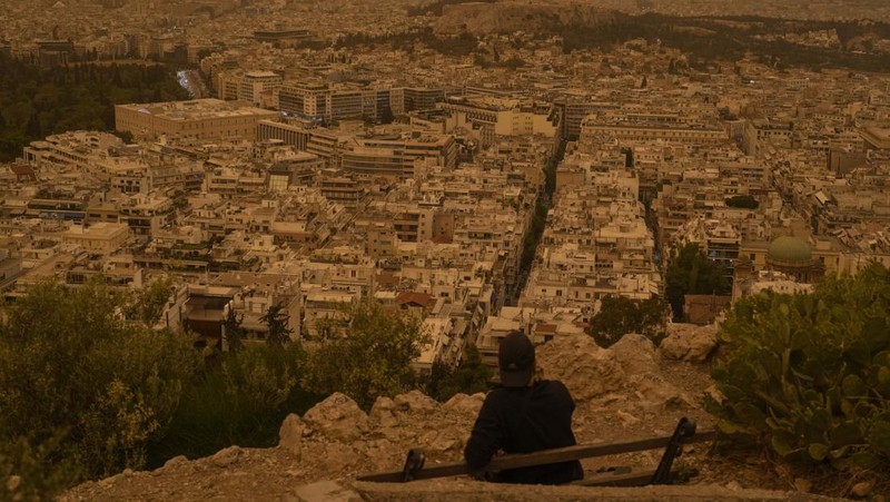 Warga mengabadikan momen gelombang debu yang tertiup angin dari gurun Sahara menutupi Athena dan kota-kota Yunani lainnya pada Selasa, (23/4/2024) waktu setempat. (AP Photo/Petros Giannakouris)