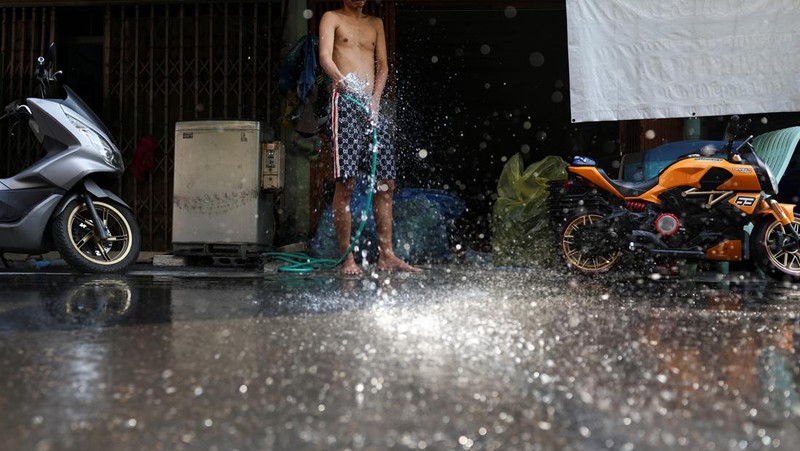 Orang-orang berjalan dengan payung melewati percikan air ketika pihak berwenang Thailand mengatakan bahwa orang-orang meninggal karena serangan panas tahun ini dan memperingatkan untuk menghindari aktivitas di luar ruangan, di Bangkok, Thailand, 5 Mei 2024. (REUTERS/Chalinee Thirasupa)