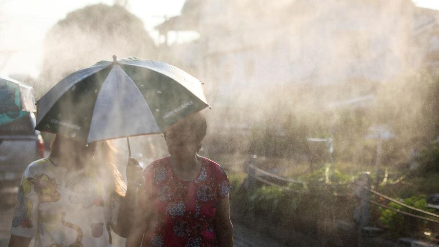 Orang-orang berjalan dengan payung melewati percikan air ketika pihak berwenang Thailand mengatakan bahwa orang-orang meninggal karena serangan panas tahun ini dan memperingatkan untuk menghindari aktivitas di luar ruangan, di Bangkok, Thailand, 5 Mei 2024. (REUTERS/Chalinee Thirasupa)