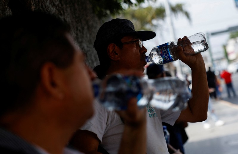 Orang-orang menutupi diri mereka dengan payung di samping orang lain saat mereka berjalan di trotoar saat suhu tinggi, di Mexico City, Meksiko 9 Mei 2024. (REUTERS/Henry Romero)