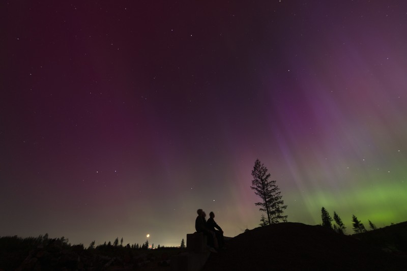 In this image taken with a long exposure, cars pass by as people look at the night sky towards the northern lights, or Aurora Borealis, on Friday, May 10, 2024, in Estacada, Ore. The National Oceanic and Atmospheric Administration issued a rare severe geomagnetic storm warning when a solar outburst reached Earth on Friday afternoon, hours sooner than anticipated. The effects were due to last through the weekend and possibly into next week. (AP Photo/Jenny Kane)