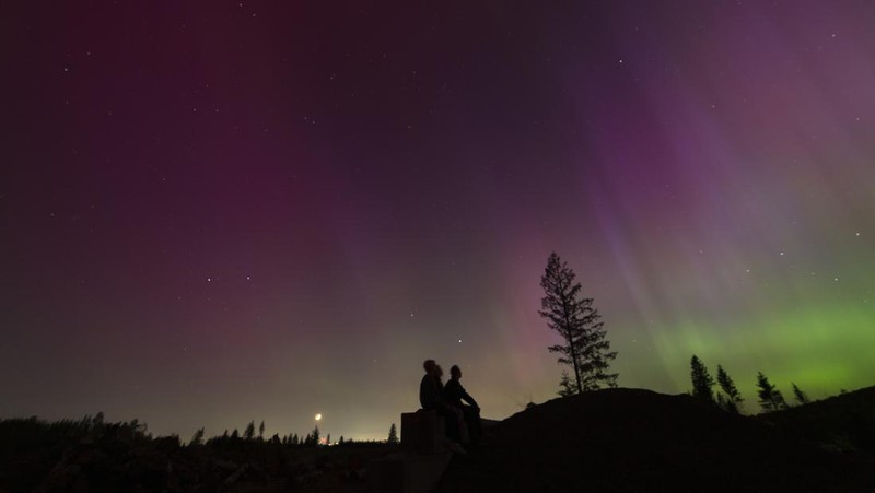 In this image taken with a long exposure, cars pass by as people look at the night sky towards the northern lights, or Aurora Borealis, on Friday, May 10, 2024, in Estacada, Ore. The National Oceanic and Atmospheric Administration issued a rare severe geomagnetic storm warning when a solar outburst reached Earth on Friday afternoon, hours sooner than anticipated. The effects were due to last through the weekend and possibly into next week. (AP Photo/Jenny Kane)