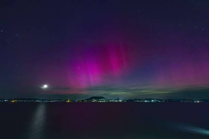 In this image taken with a long exposure, cars pass by as people look at the night sky towards the northern lights, or Aurora Borealis, on Friday, May 10, 2024, in Estacada, Ore. The National Oceanic and Atmospheric Administration issued a rare severe geomagnetic storm warning when a solar outburst reached Earth on Friday afternoon, hours sooner than anticipated. The effects were due to last through the weekend and possibly into next week. (AP Photo/Jenny Kane)