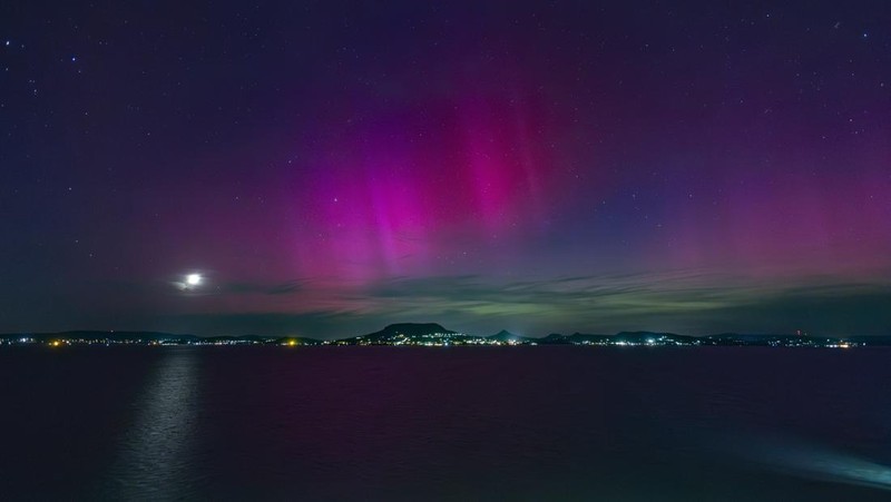 In this image taken with a long exposure, cars pass by as people look at the night sky towards the northern lights, or Aurora Borealis, on Friday, May 10, 2024, in Estacada, Ore. The National Oceanic and Atmospheric Administration issued a rare severe geomagnetic storm warning when a solar outburst reached Earth on Friday afternoon, hours sooner than anticipated. The effects were due to last through the weekend and possibly into next week. (AP Photo/Jenny Kane)