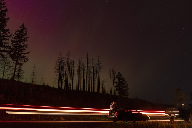 In this image taken with a long exposure, cars pass by as people look at the night sky towards the northern lights, or Aurora Borealis, on Friday, May 10, 2024, in Estacada, Ore. The National Oceanic and Atmospheric Administration issued a rare severe geomagnetic storm warning when a solar outburst reached Earth on Friday afternoon, hours sooner than anticipated. The effects were due to last through the weekend and possibly into next week. (AP Photo/Jenny Kane)