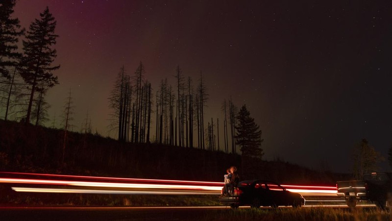 In this image taken with a long exposure, cars pass by as people look at the night sky towards the northern lights, or Aurora Borealis, on Friday, May 10, 2024, in Estacada, Ore. The National Oceanic and Atmospheric Administration issued a rare severe geomagnetic storm warning when a solar outburst reached Earth on Friday afternoon, hours sooner than anticipated. The effects were due to last through the weekend and possibly into next week. (AP Photo/Jenny Kane)