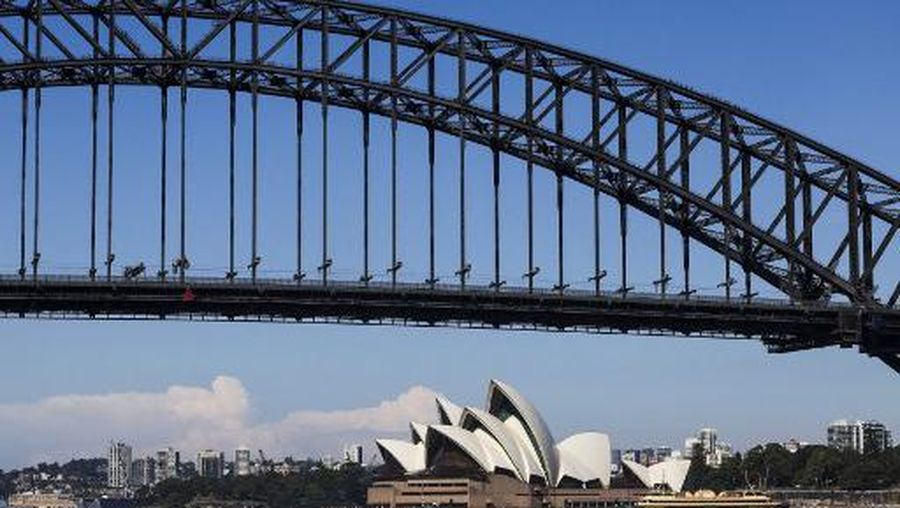 A ferry passes the Sydney Opera House as flags atop the Sydney Harbour Bridge fly at half-mast on April 15, 2024, as a mark of respect for the victims of the Westfield Bondi Junction shopping mall attack. A 40-year-old knifeman with mental illness roamed the packed shopping centre on April 13, killing six people and seriously wounding a dozen others. (Photo by DAVID GRAY / AFP)